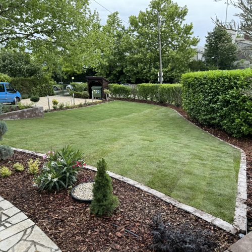 Precisely cut lawn with a border all around, with a driveway in the distance.